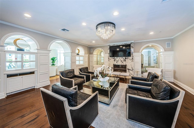 living room with a high end fireplace, ornamental molding, decorative columns, a notable chandelier, and hardwood / wood-style flooring