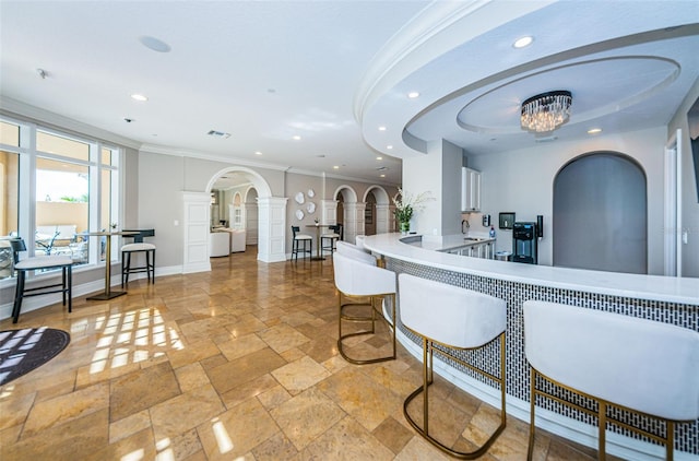 kitchen with crown molding, a kitchen breakfast bar, a chandelier, light tile flooring, and ornate columns