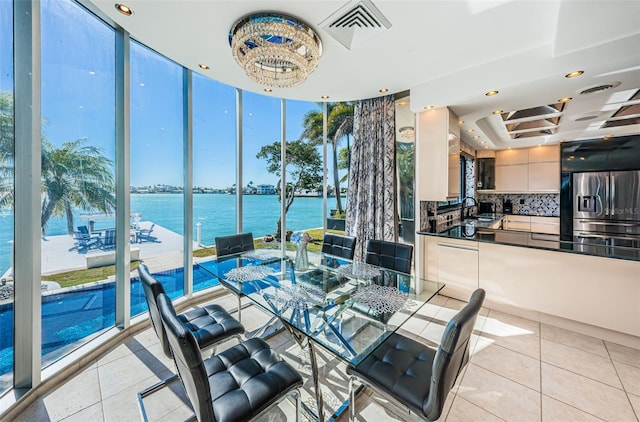 dining area featuring light tile flooring, floor to ceiling windows, a water view, a tray ceiling, and sink