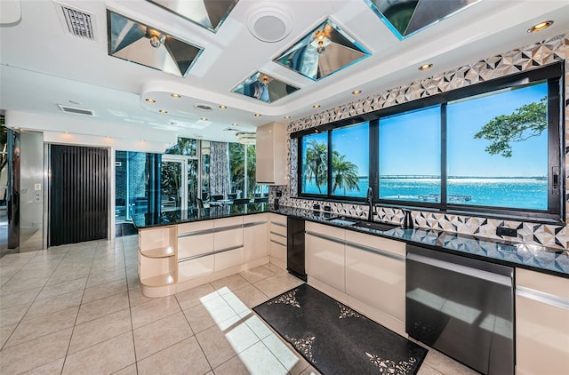 kitchen with light tile flooring, sink, a water view, dark stone counters, and stainless steel dishwasher