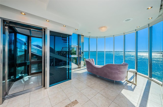 interior space featuring light tile flooring, a water view, and a wall of windows