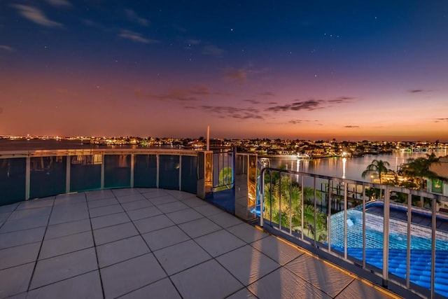 patio terrace at dusk featuring a water view and a balcony