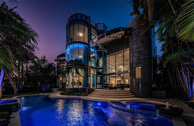 pool at dusk featuring an in ground hot tub and pool water feature