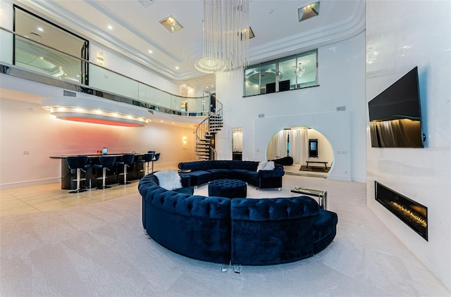 carpeted living room with a bar, a towering ceiling, stairway, and a glass covered fireplace