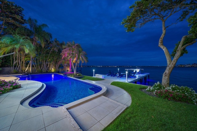 pool at night featuring a water view, an outdoor pool, a patio, and a yard