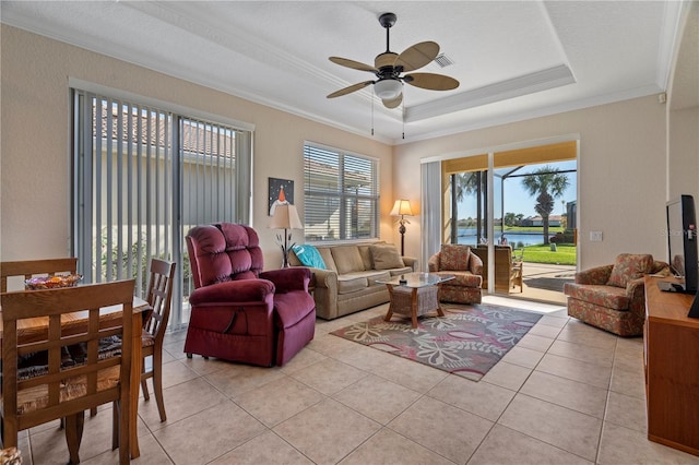 living room with a tray ceiling, ceiling fan, a water view, light tile floors, and crown molding