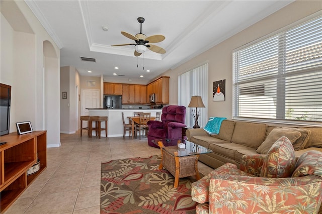 living room featuring a raised ceiling, ornamental molding, ceiling fan, and light tile floors