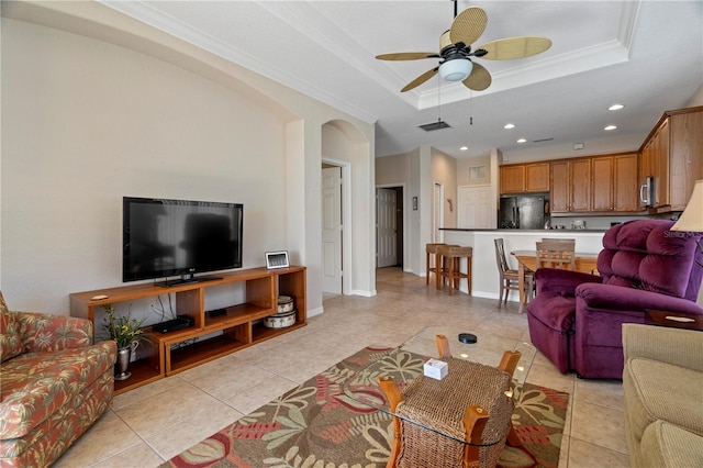 living room with a raised ceiling, ceiling fan, light tile floors, and ornamental molding