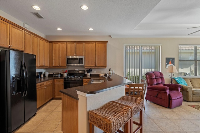 kitchen featuring light tile flooring, a kitchen bar, ceiling fan, black appliances, and sink