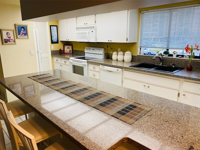 kitchen with sink, a breakfast bar area, white appliances, and white cabinetry