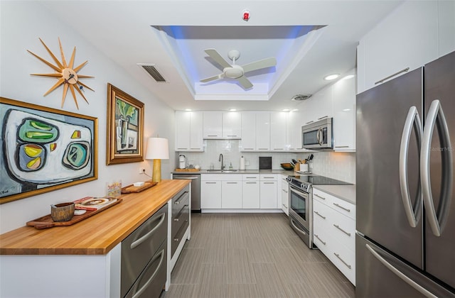 kitchen with ceiling fan, stainless steel appliances, white cabinets, a raised ceiling, and tasteful backsplash