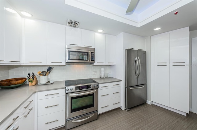 kitchen with tasteful backsplash, white cabinets, appliances with stainless steel finishes, and dark tile floors