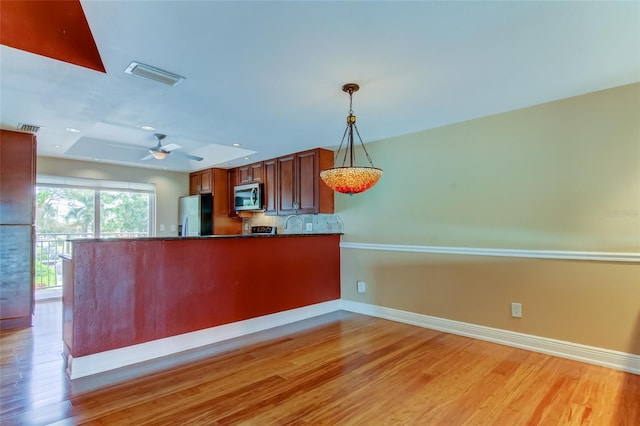 kitchen with appliances with stainless steel finishes, pendant lighting, tasteful backsplash, and light wood-type flooring