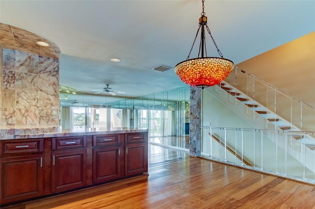 kitchen featuring light stone counters, hanging light fixtures, ceiling fan with notable chandelier, and light hardwood / wood-style flooring