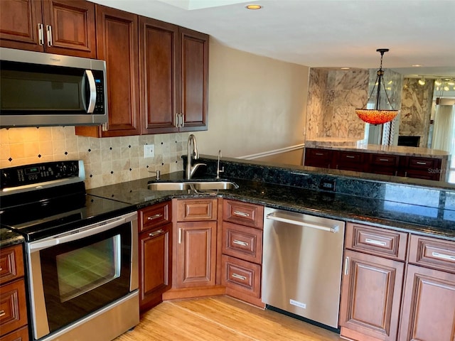 kitchen with hanging light fixtures, sink, light wood-type flooring, stainless steel appliances, and dark stone counters