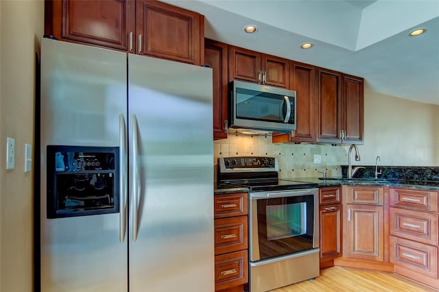 kitchen featuring sink, dark stone countertops, light hardwood / wood-style flooring, backsplash, and stainless steel appliances