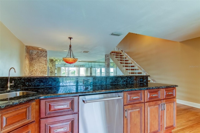 kitchen featuring stainless steel dishwasher, pendant lighting, dark stone counters, light hardwood / wood-style flooring, and sink