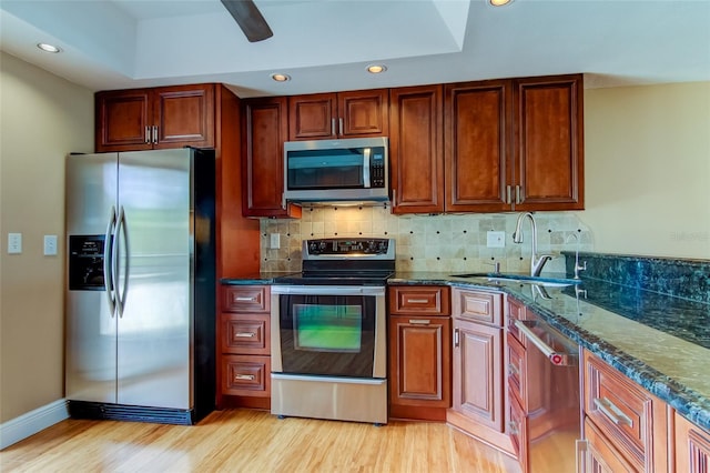 kitchen with ceiling fan, dark stone counters, appliances with stainless steel finishes, backsplash, and light hardwood / wood-style floors