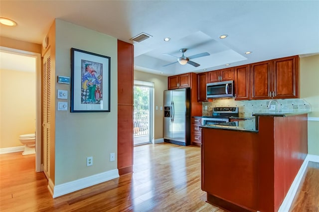 kitchen with appliances with stainless steel finishes, backsplash, ceiling fan, and light wood-type flooring