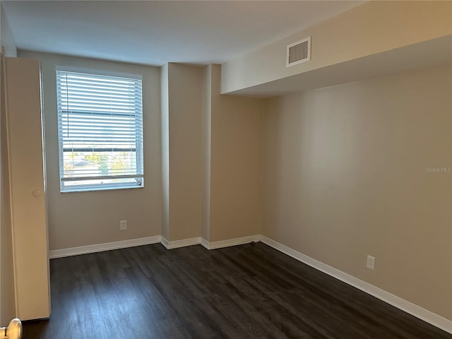 empty room featuring visible vents, baseboards, and dark wood finished floors