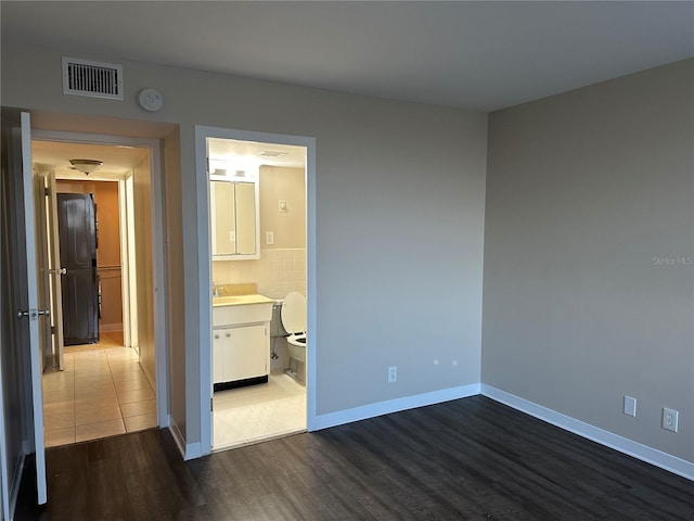 unfurnished bedroom with a sink, visible vents, baseboards, and dark wood-style floors