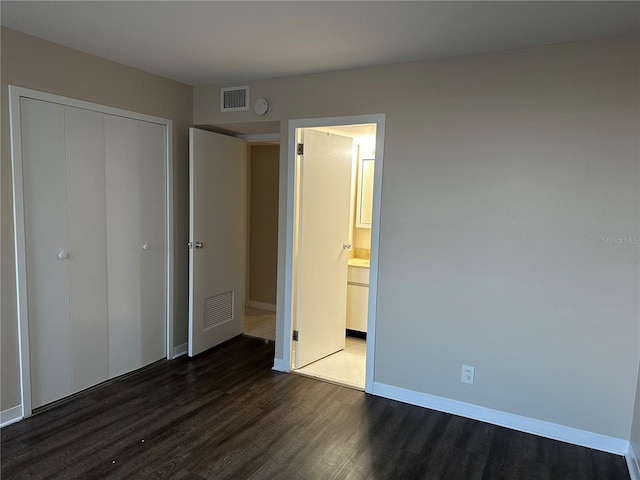 unfurnished bedroom featuring visible vents, ensuite bath, wood finished floors, a closet, and baseboards