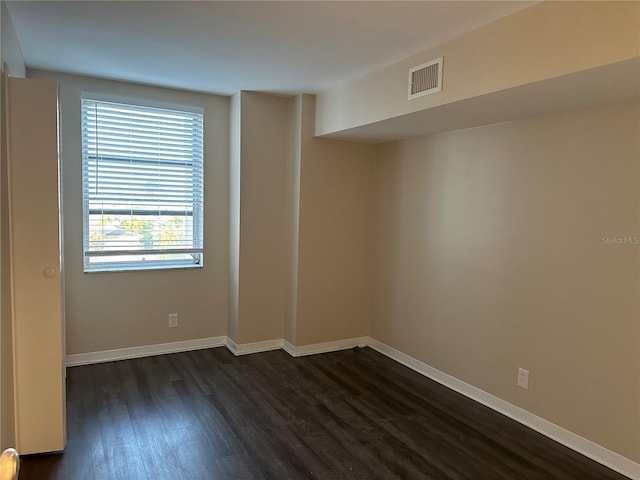 spare room featuring dark wood-style floors, visible vents, and baseboards