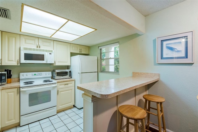 kitchen with kitchen peninsula, light tile flooring, white appliances, a kitchen breakfast bar, and cream cabinets