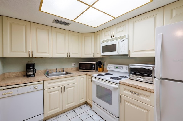 kitchen featuring light tile floors, white appliances, cream cabinets, and sink