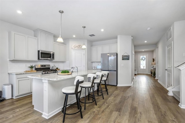 kitchen with decorative light fixtures, appliances with stainless steel finishes, an island with sink, light stone countertops, and white cabinets