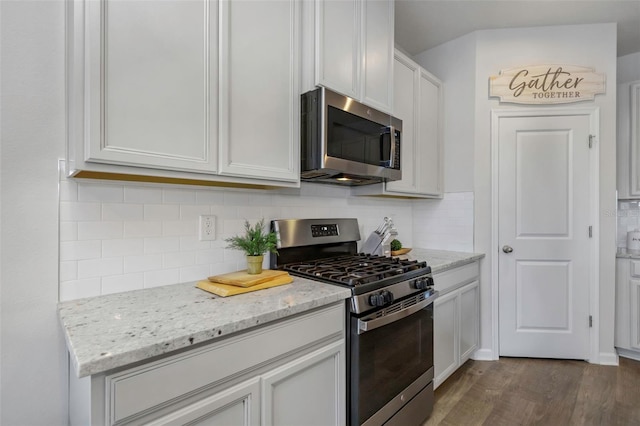 kitchen with appliances with stainless steel finishes, tasteful backsplash, light stone countertops, white cabinets, and dark hardwood / wood-style flooring