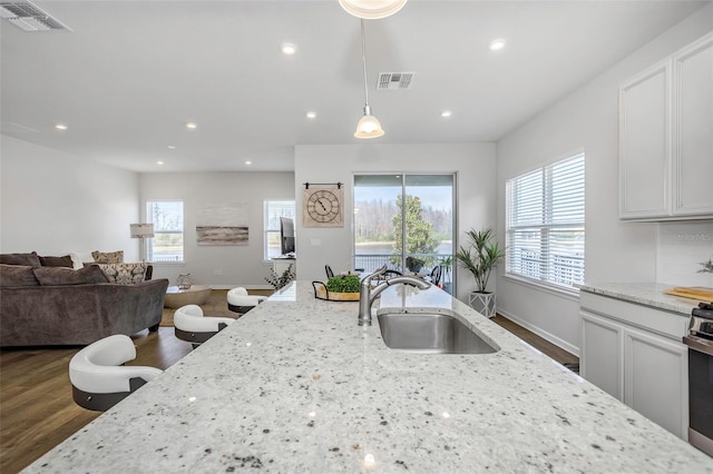 kitchen with pendant lighting, white cabinetry, sink, light stone counters, and dark wood-type flooring