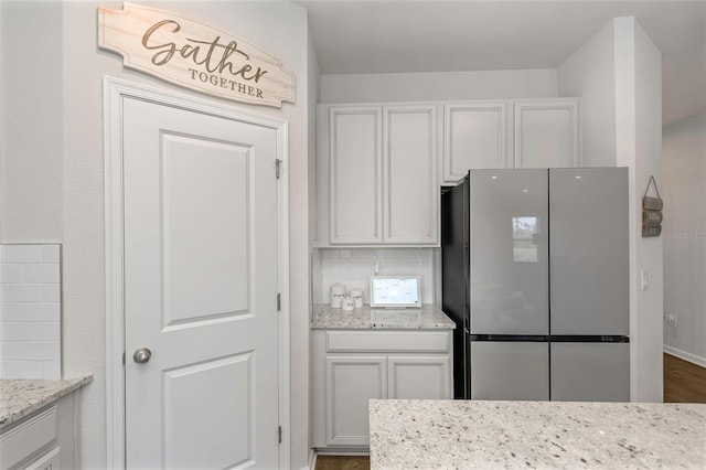 kitchen featuring white cabinetry, light stone counters, stainless steel fridge, and tasteful backsplash