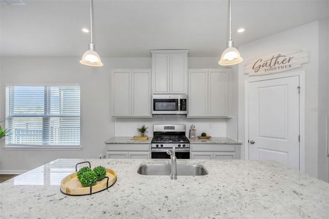 kitchen with sink, appliances with stainless steel finishes, white cabinetry, hanging light fixtures, and light stone counters