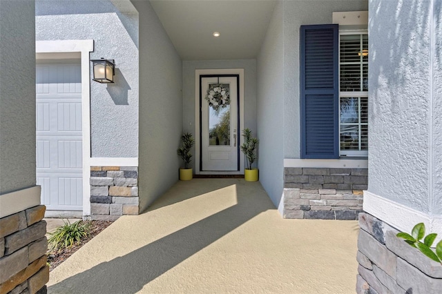 view of exterior entry with stone siding, stucco siding, and a garage