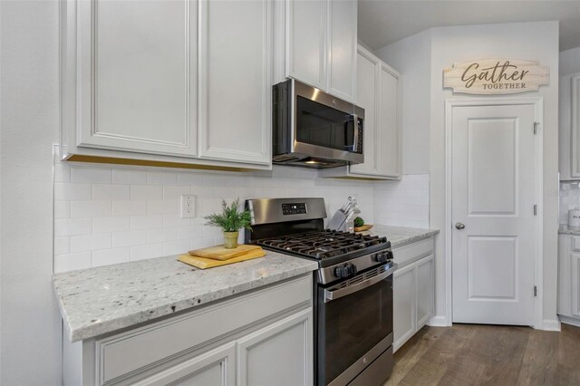 kitchen featuring light stone counters, dark wood-style floors, appliances with stainless steel finishes, white cabinetry, and backsplash