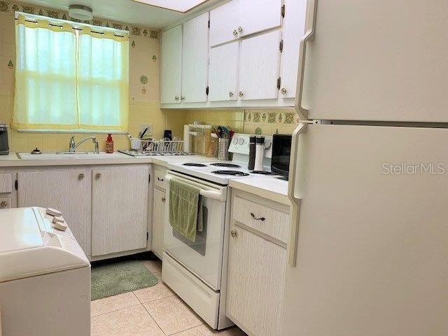 kitchen featuring white appliances, sink, white cabinets, and light tile floors