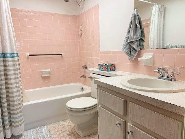 full bathroom with large vanity, shower / bathtub combination with curtain, tasteful backsplash, and tile walls