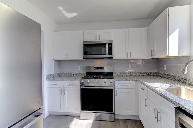 kitchen featuring backsplash, light hardwood / wood-style floors, appliances with stainless steel finishes, and white cabinetry