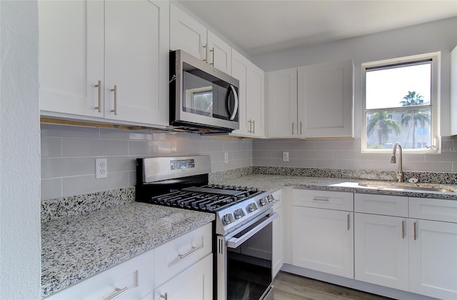 kitchen featuring white cabinetry, appliances with stainless steel finishes, sink, light hardwood / wood-style flooring, and tasteful backsplash