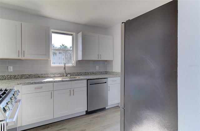 kitchen with sink, white cabinets, appliances with stainless steel finishes, backsplash, and light hardwood / wood-style floors