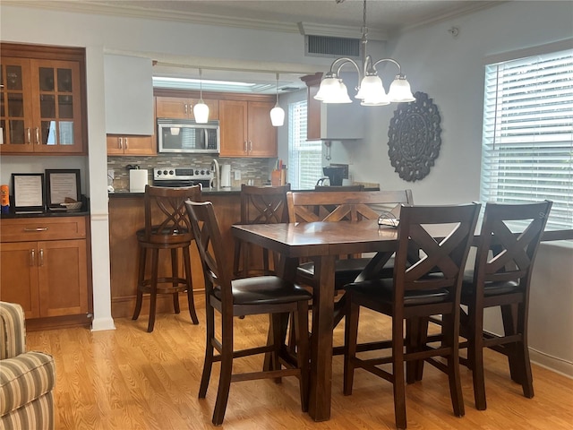 dining room with light hardwood / wood-style floors, a chandelier, a healthy amount of sunlight, and crown molding