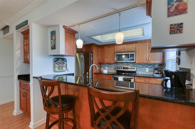 kitchen with pendant lighting, kitchen peninsula, appliances with stainless steel finishes, and ornamental molding