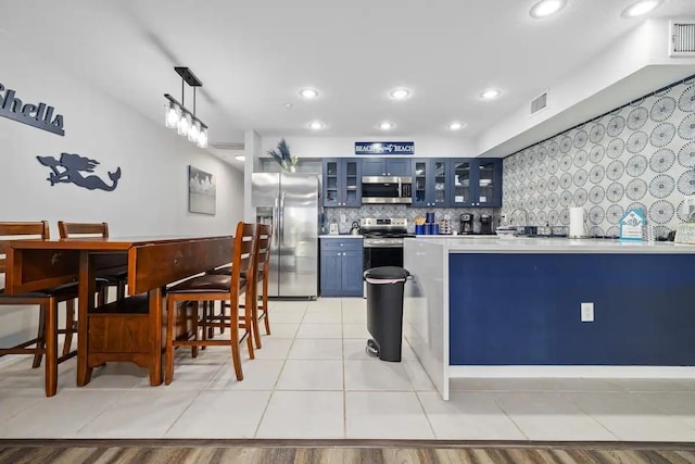 kitchen featuring blue cabinets, pendant lighting, light tile floors, stainless steel appliances, and tasteful backsplash