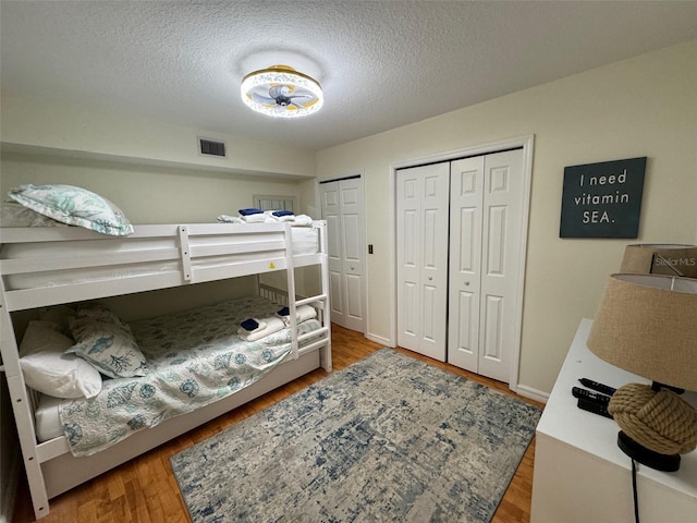 bedroom featuring two closets, a textured ceiling, and hardwood / wood-style flooring