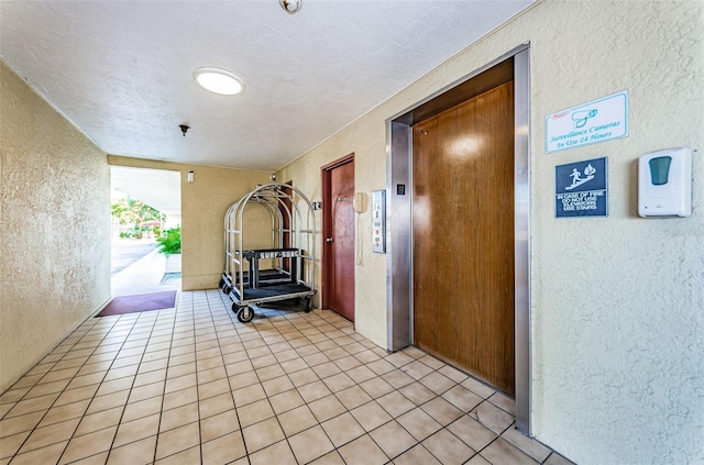 corridor with a textured ceiling, light tile floors, and elevator