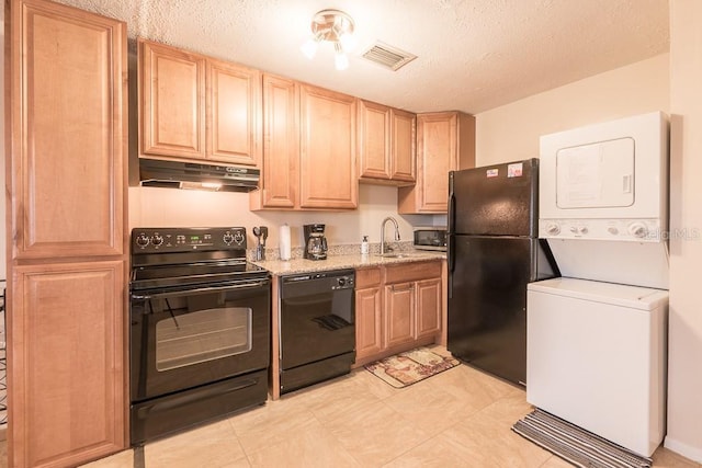 kitchen with sink, stacked washer / drying machine, light stone counters, black appliances, and a textured ceiling