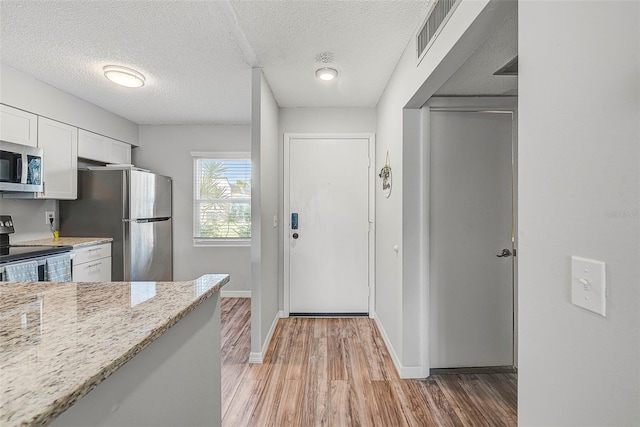 kitchen with stainless steel appliances, light stone countertops, a textured ceiling, light hardwood / wood-style flooring, and white cabinets