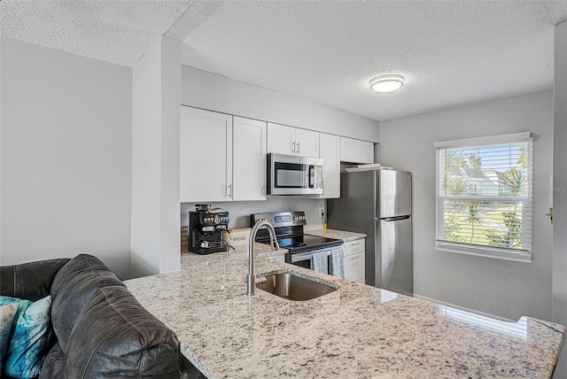 kitchen featuring kitchen peninsula, white cabinets, appliances with stainless steel finishes, light stone countertops, and a textured ceiling