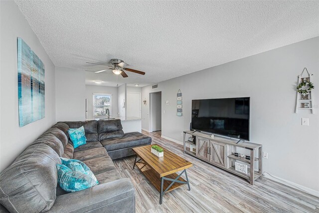 living room with light hardwood / wood-style floors, ceiling fan, and a textured ceiling